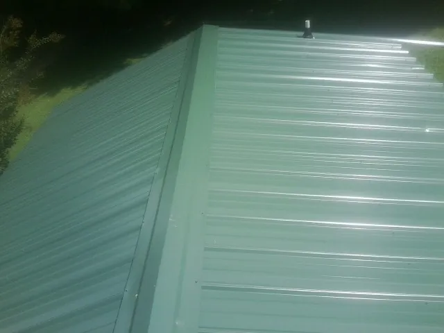 New green metal panels meeting at the ridge of a roof — Flat Roof Repair work by our crew in Vinton